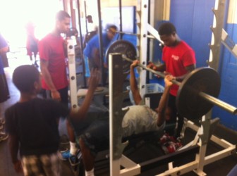 Romelle Person spots for Jordan Goliday in the MRH weight room. Darren Williams waits his turn.