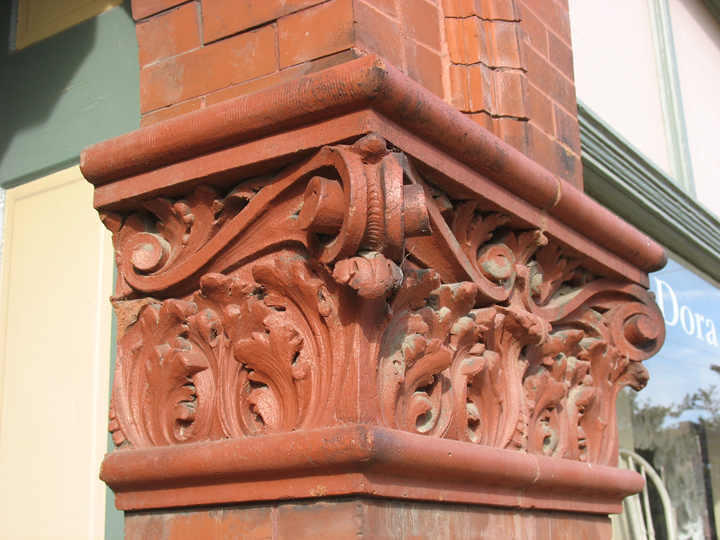 The capital on this brick pillar is an example of some of the finest terra cotta in Maplewood. The pillar supports a brick arch over the entrys to the second floor apartments. The arch has a limestone keystone. The design of the capital looks like acanthus leaves topped with scroll work. Two architectural motifs that are positively ancient. Look closely at the top and bottom half round moldings. You can see the lines of a rake, a common clay tool that a worker used to score the clay in order to give it more texture. 